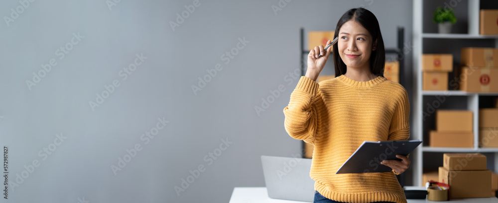 Happy young online business shop owner writing down the e-commerce details on the board while prepar