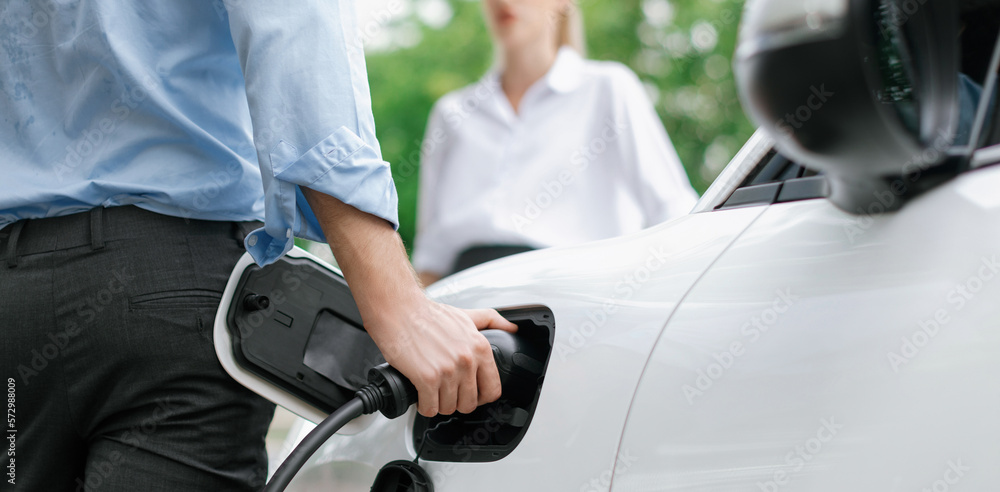 Closeup focus hand insert EV charger to electric vehicle at public charging point in car park with b