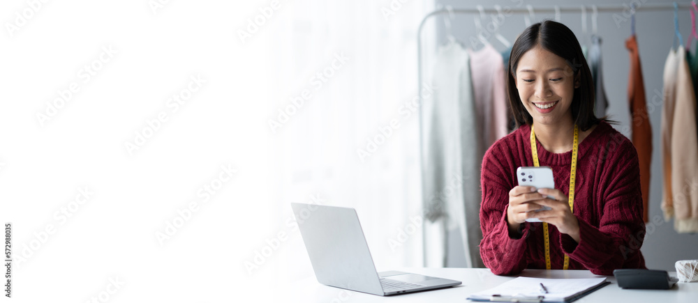 Young Asian cloth shop owner using smartphone while working in her modern studio.