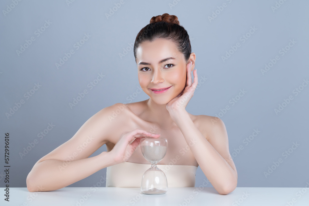 Glamorous model holding hourglass in beauty concept of anti-aging skincare treatment for woman. Youn