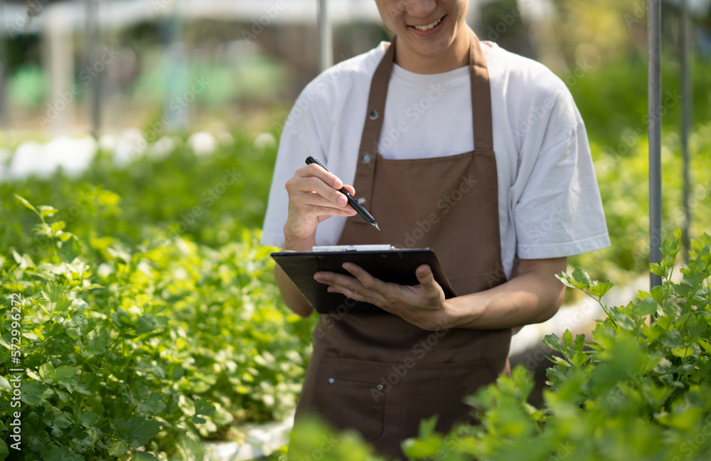 Young handsome Asian farm worker working in the farm while collect and write data on the document.