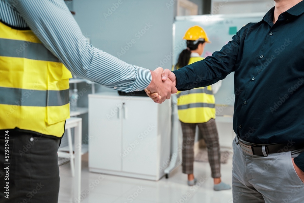 An engineer with a protective vest handshake with an investor in his office. Following a successful 