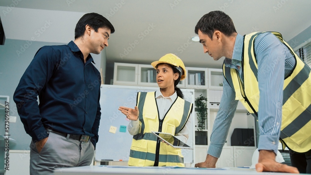 Engineers and competent employer discussing plans and blueprints together with tablet in the office.