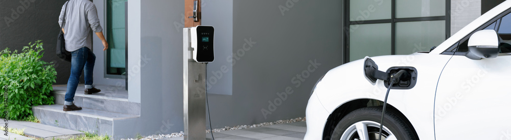 Progressive asian man and electric car with home charging station. Concept of the use of electric ve