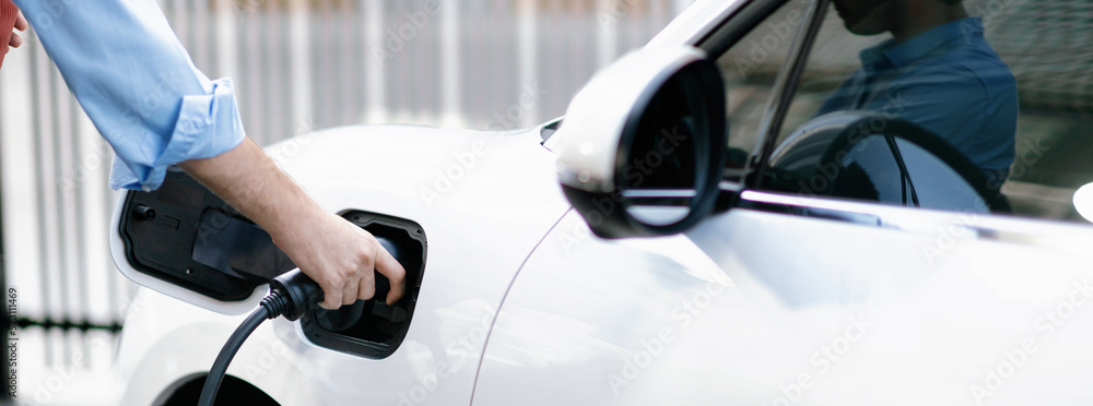 Closeup progressive man holding EV charger plug from public charging station for electric vehicle wi