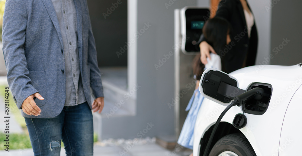 Closeup focus hand insert EV charger plug to electric vehicle at home charging station with blurred 