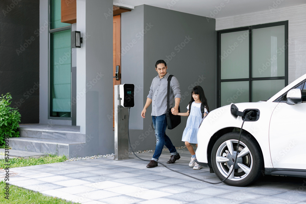 Progressive father and daughter plugs EV charger from home charging station to electric vehicle. Fut