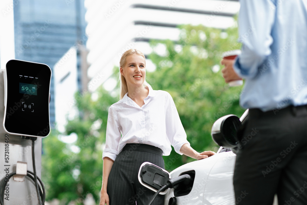 Progressive businessman and businesswoman with electric car parking and connected to public charging