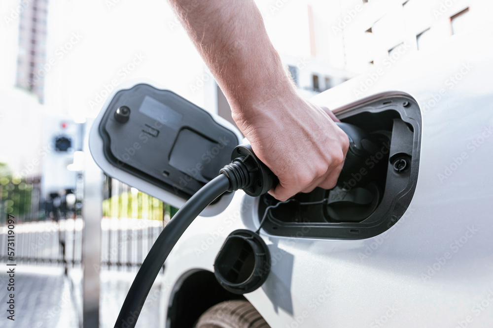 Closeup progressive man holding EV charger plug from public charging station for electric vehicle wi