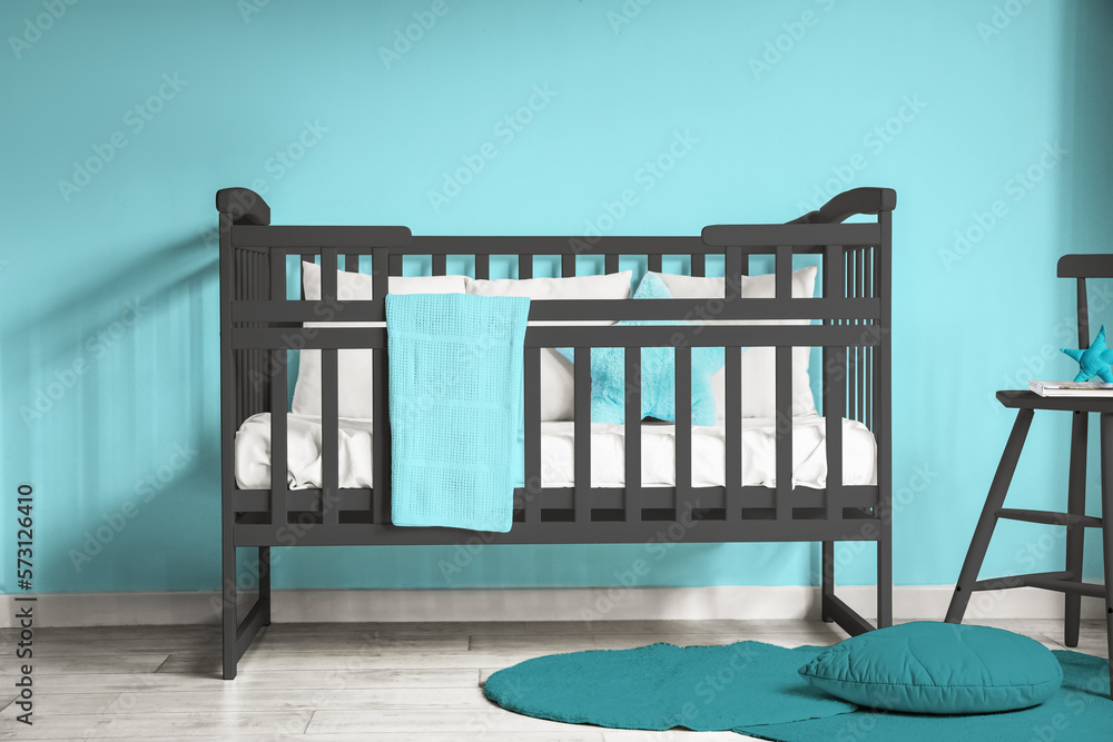 Comfortable crib near blue wall in childrens room interior