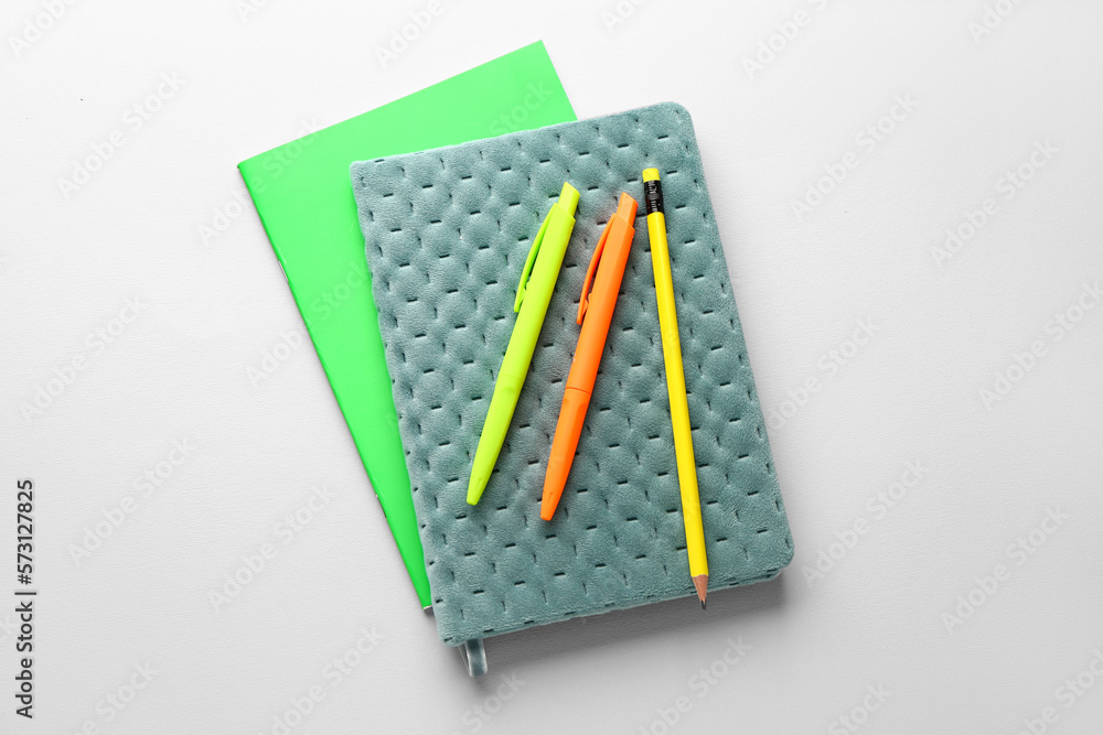 Notebooks, pens and pencil on light background