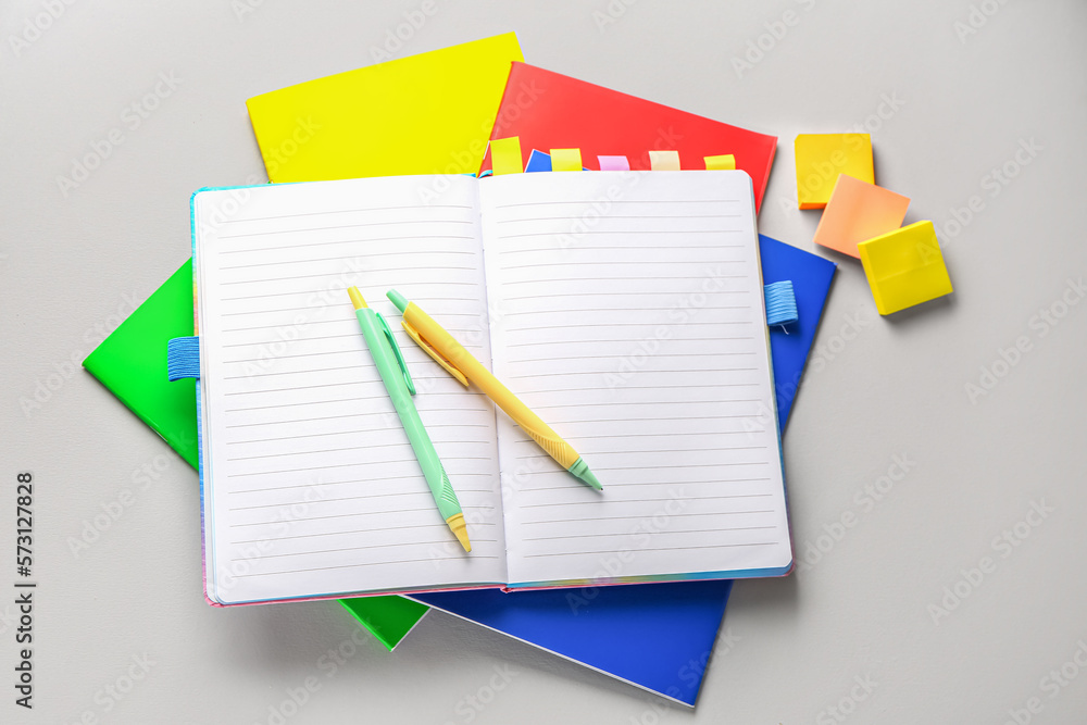 Different notebooks, sticky notes and pens on light background