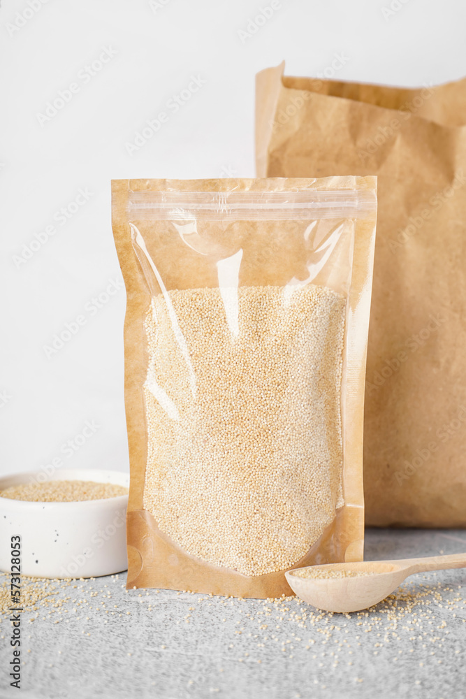 Paper bag, bowl and spoon of amaranth seeds on table, closeup