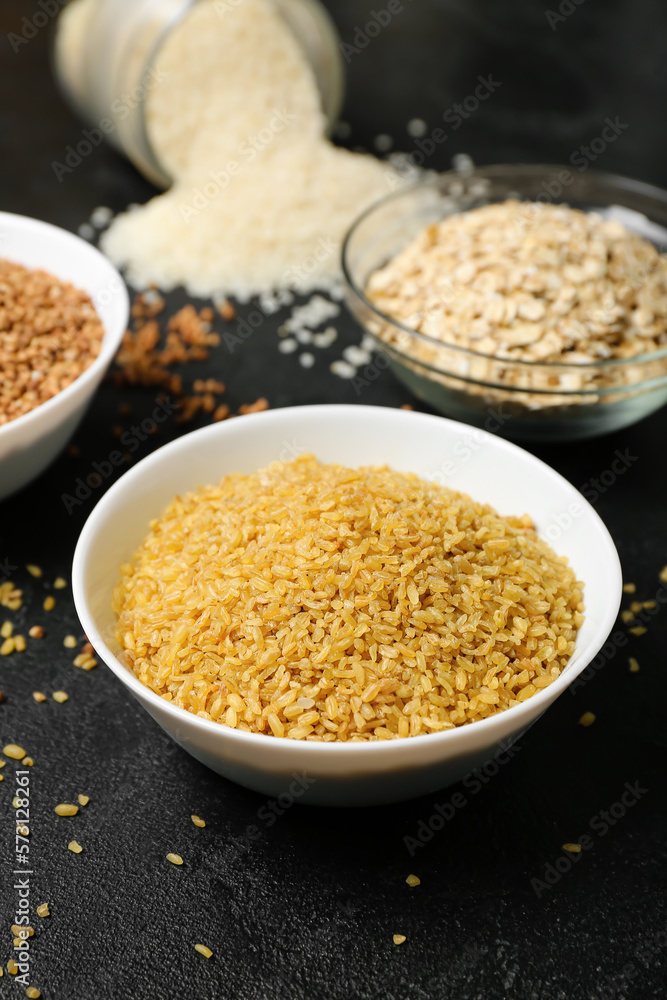 Bowl of raw bulgur on dark background, closeup