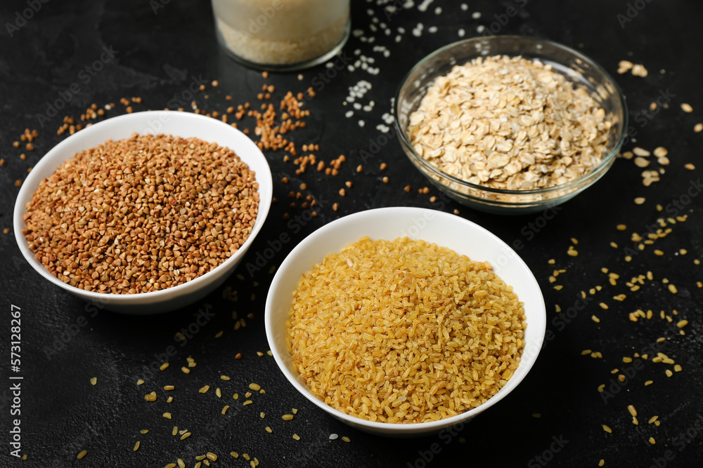 Bowls with bulgur, buckwheat and oatmeal on dark background