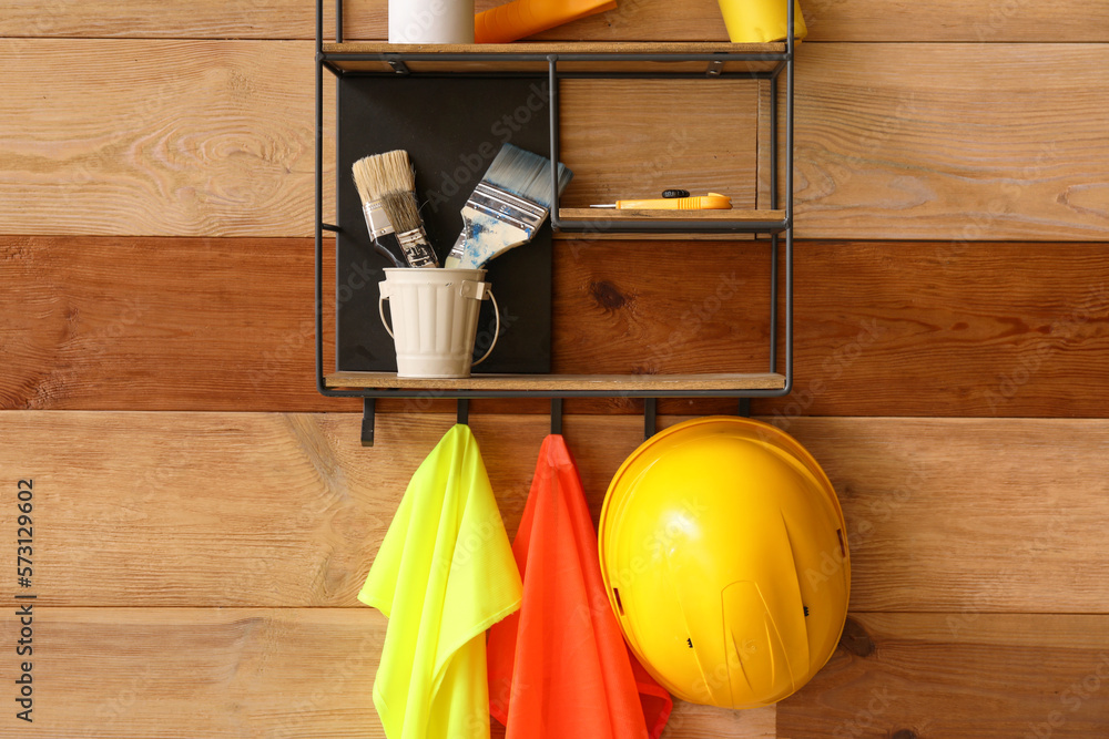 Shelf with builders supplies and reflective vests on wooden wall