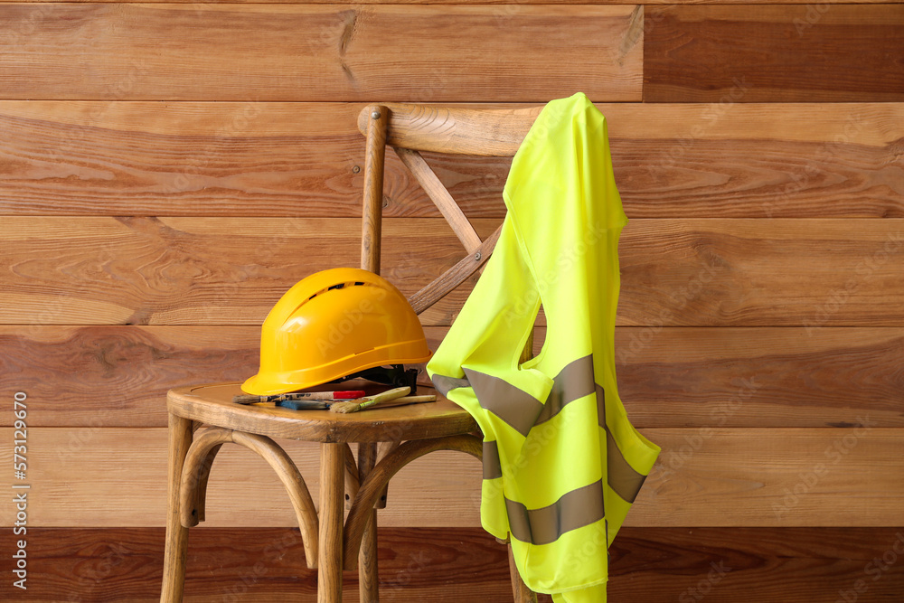 Chair with hardhat and reflective vest near wooden wall