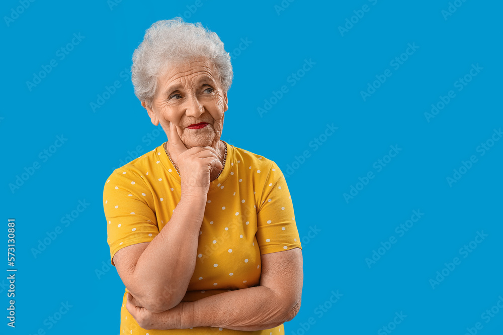 Thoughtful senior woman in yellow t-shirt on blue background