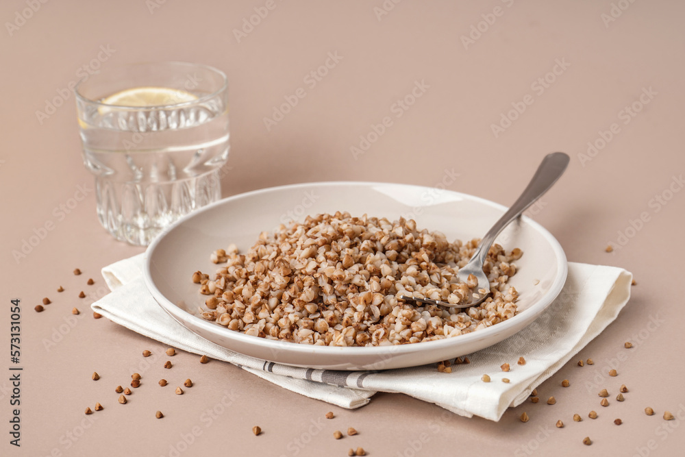 Napkin with plate of tasty buckwheat porridge and glass of water with lemon on beige background