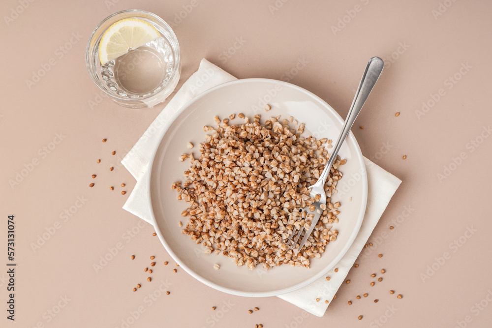 Napkin with plate of tasty buckwheat porridge and glass of water with lemon on beige background