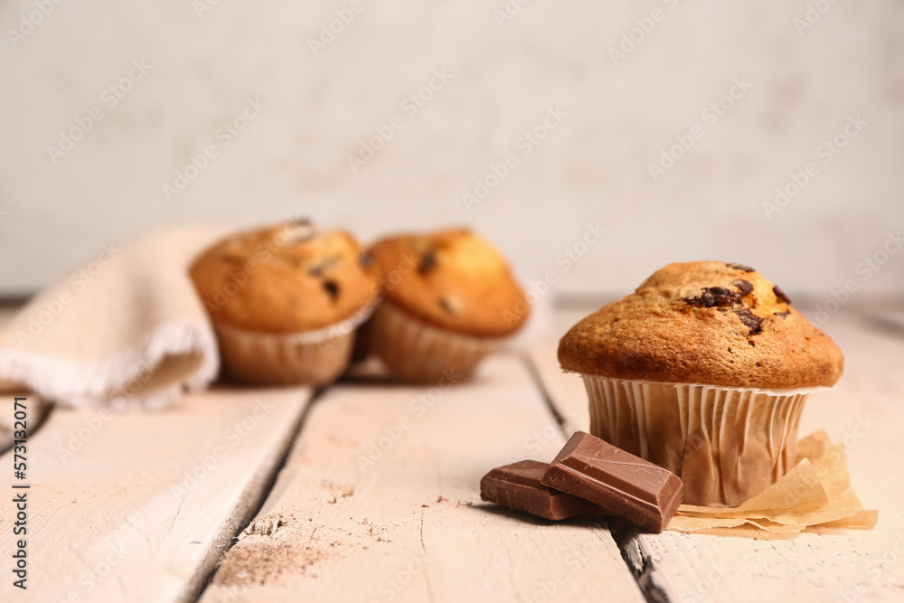 Tasty muffin and pieces of chocolate on light wooden table