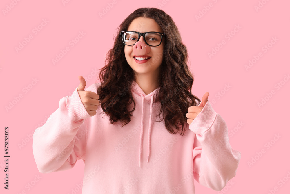 Teenage girl in funny disguise showing thumbs-up on pink background. April Fools Day celebration