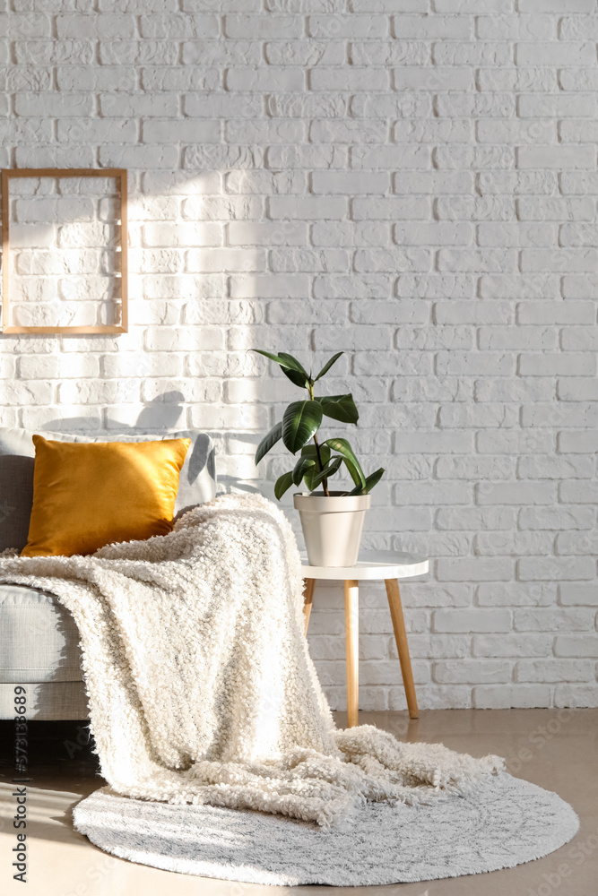 Table with houseplant and grey couch near white brick wall in living room