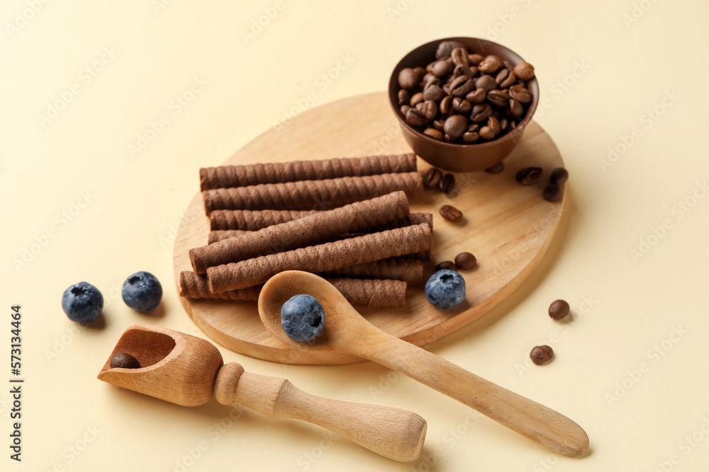 Board with delicious chocolate wafer rolls, coffee beans and blueberries on beige background