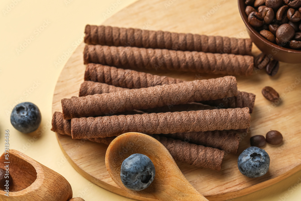 Board with delicious chocolate wafer rolls, coffee beans and blueberries on beige background, closeu