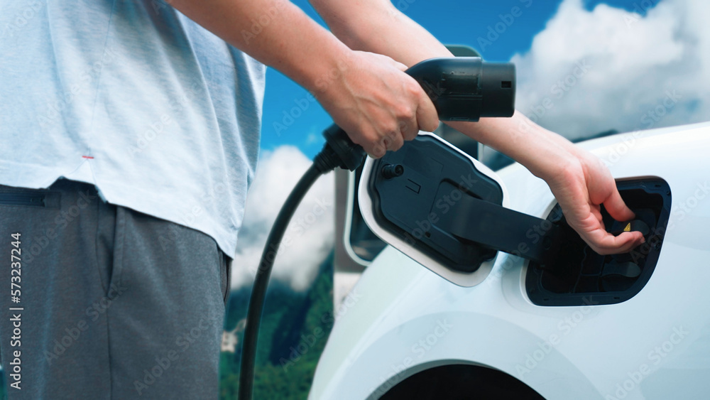 Progressive man recharge electric vehicle installing power cable plug from charging station with rur