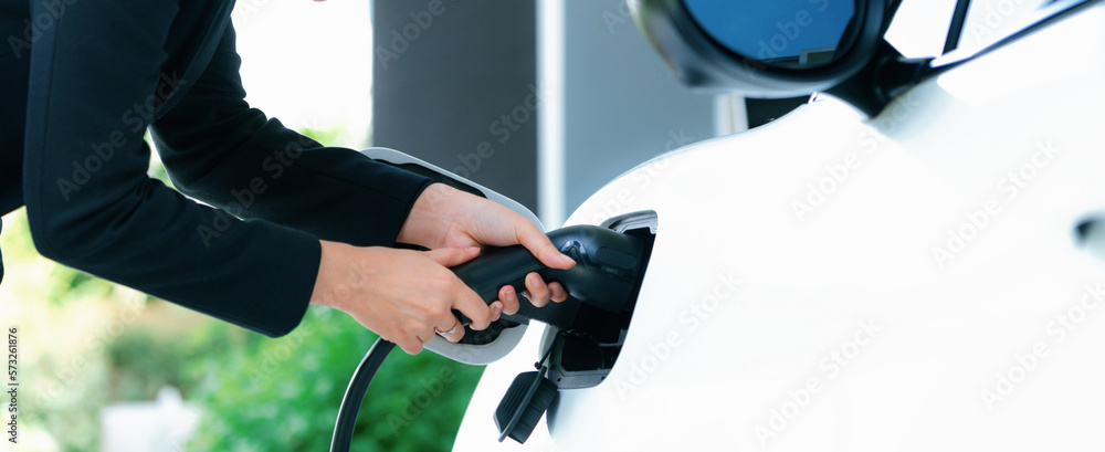 Closeup progressive woman install cable plug to her electric car with home charging station. Concept