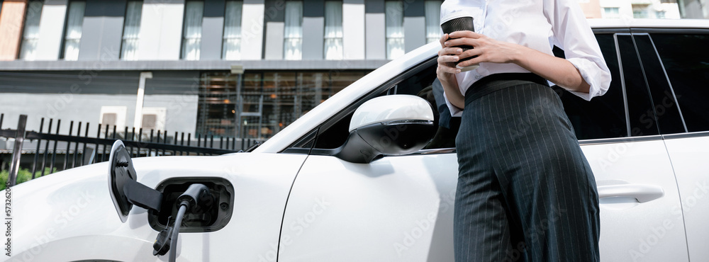 Closeup progressive suit-clad businesswoman with her electric vehicle recharge her car on public cha