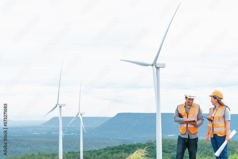 Male and female engineers working on a wind farm atop a hill or mountain in the rural. Progressive i