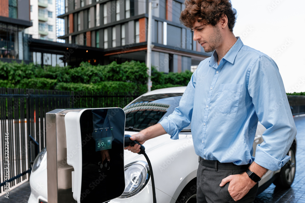 Progressive businessman insert charger plug from charging station to his electric vehicle with apart