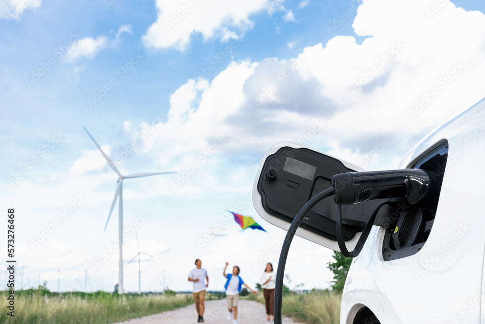 Concept of progressive happy family holding windmill toy and relax at wind farm with electric vehicl