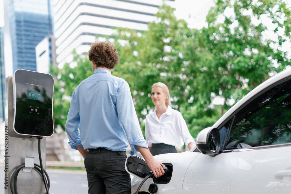 Progressive businessman and businesswoman with electric car parking and connected to public charging