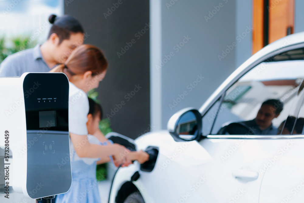 Closeup focus hand insert EV charger plug to electric vehicle at home charging station with blurred 