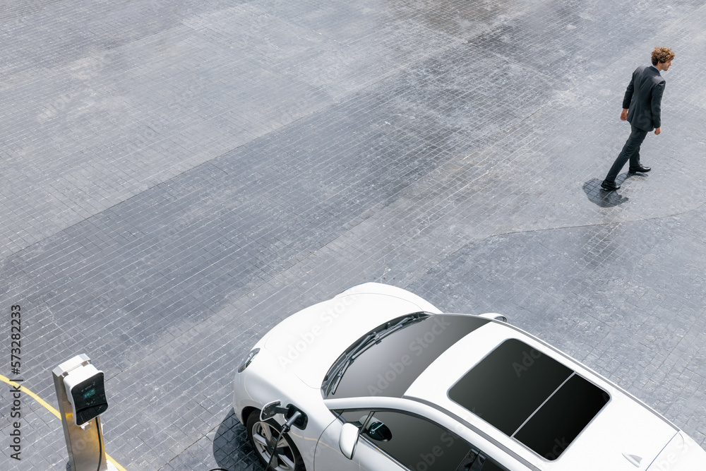 Aerial view of progressive businessman in black formal suit with his electric vehicle recharging bat