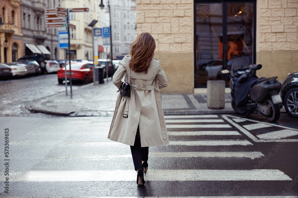 Woman in trendy outfits crosses road against backdrop of city buildings. High quality photo