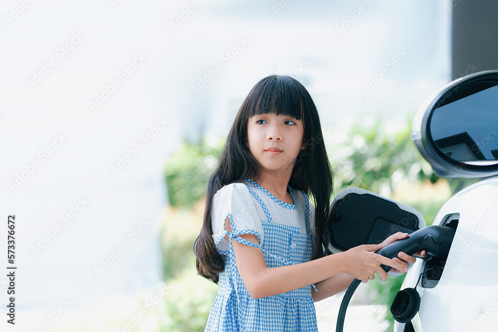 A playful girl holding an EV plug, a home charging station providing a sustainable power source for 