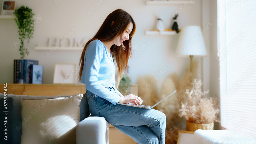 Young asian woman using laptop while seated on couch at home