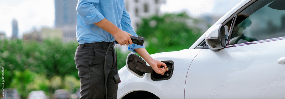 Closeup progressive man holding EV charger plug from public charging station for electric vehicle wi