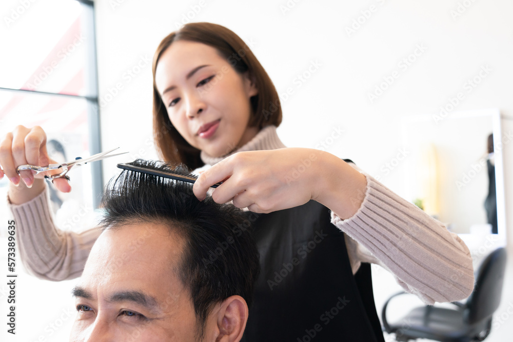 Closeup asian female barber making haircut for male customer with male hairstyle in qualified barber