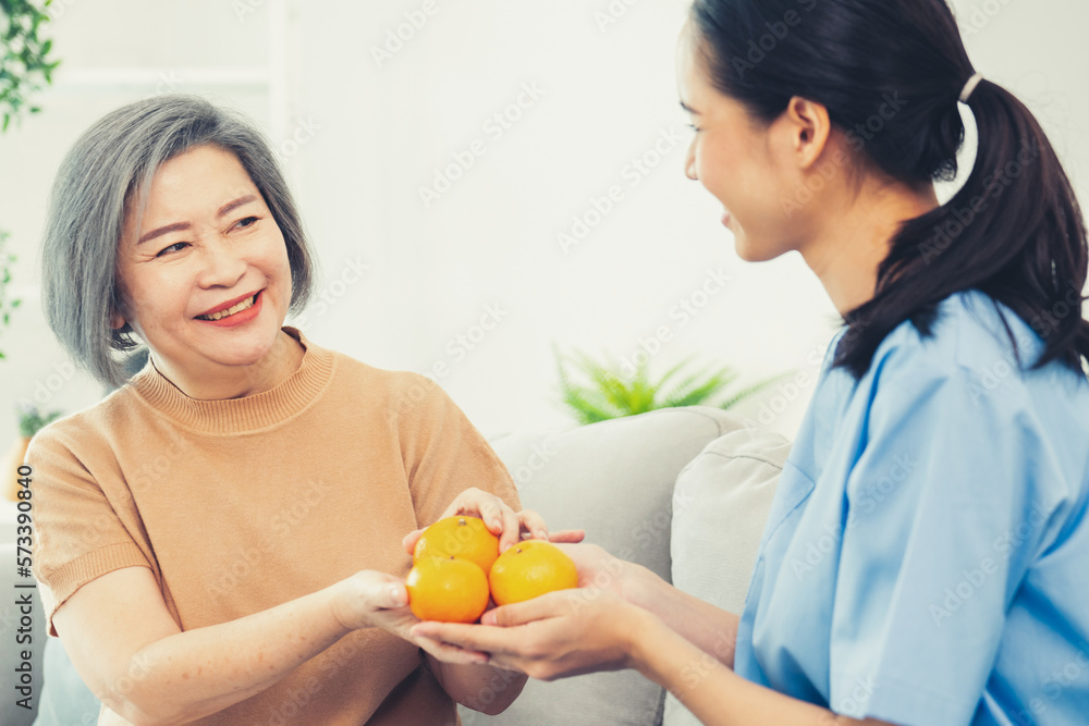 A young caregiver handing oranges to her contented senior patient at the living room. Senior care se