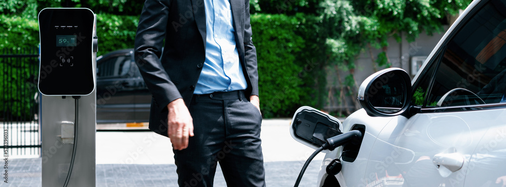 Closeup progressive suit-clad businessman with his electric vehicle recharge his car on public charg