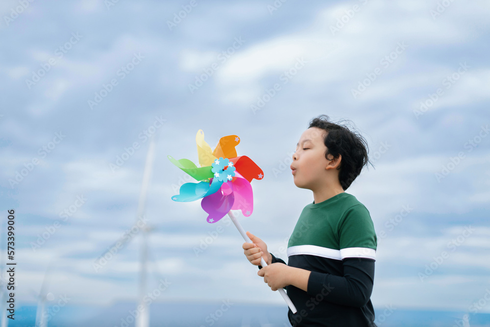 Progressive young asian boy playing with wind pinwheel toy in the wind turbine farm, green field ove