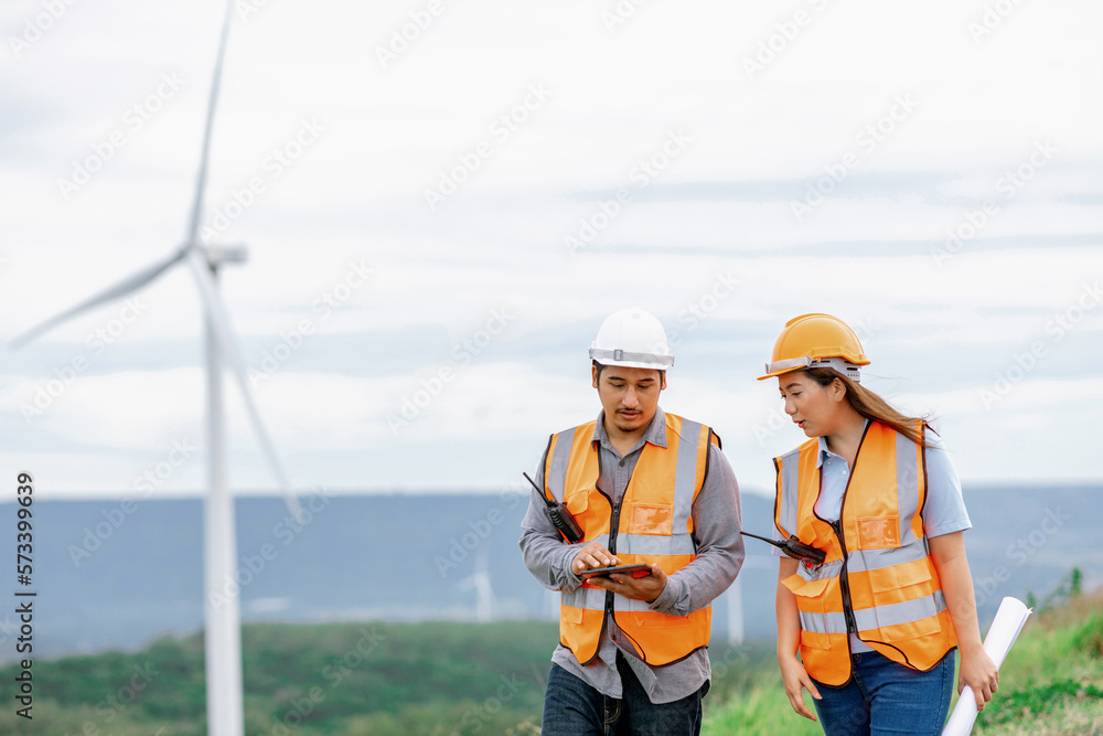 Male and female engineers working on a wind farm atop a hill or mountain in the rural. Progressive i