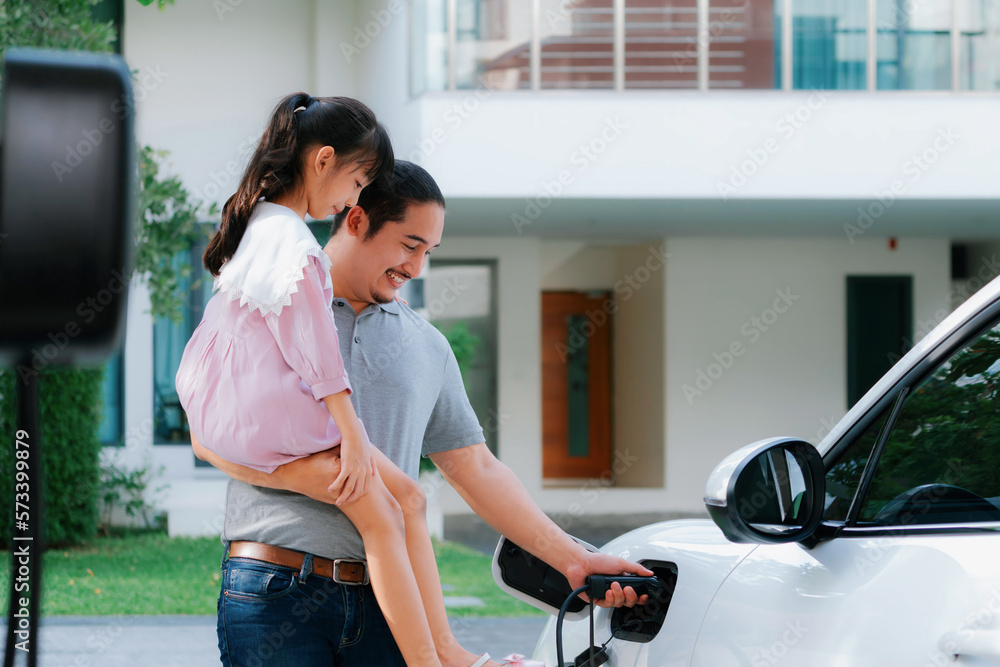 Progressive father and daughter returned from school in electric vehicle that is being charged at ho