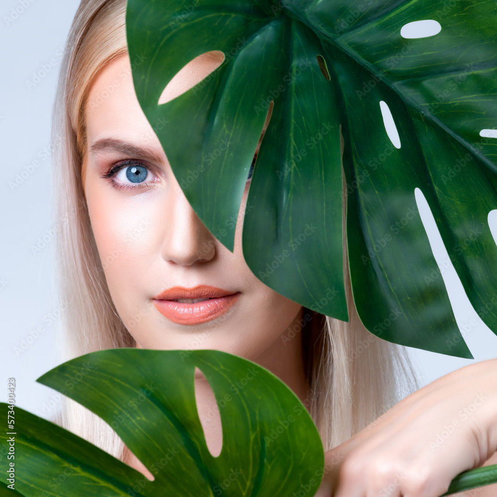 Closeup facial portrait personable woman with perfect smooth makeup holding green monstera leaves an