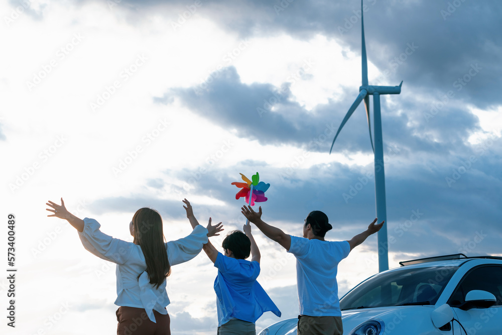 Concept of progressive happy family enjoying their time at wind farm with electric vehicle. Electric